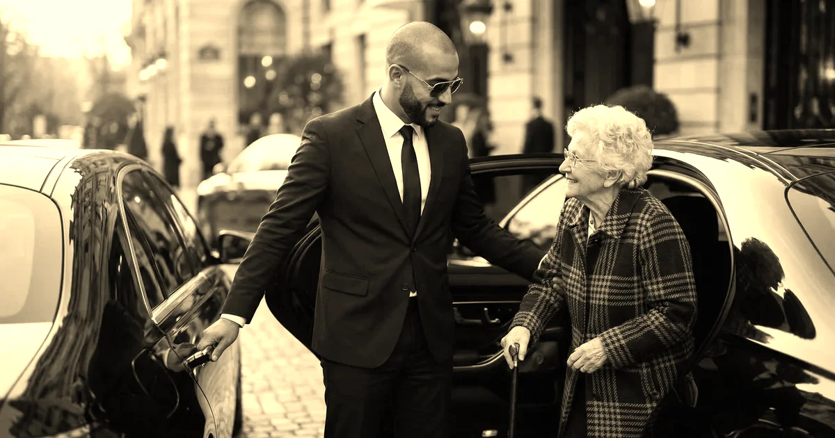 Chauffeur en costume sombre aidant une cliente âgée à descendre d'une berline noire devant un hôtel parisien à l'heure dorée, traitement sépia presse B2B