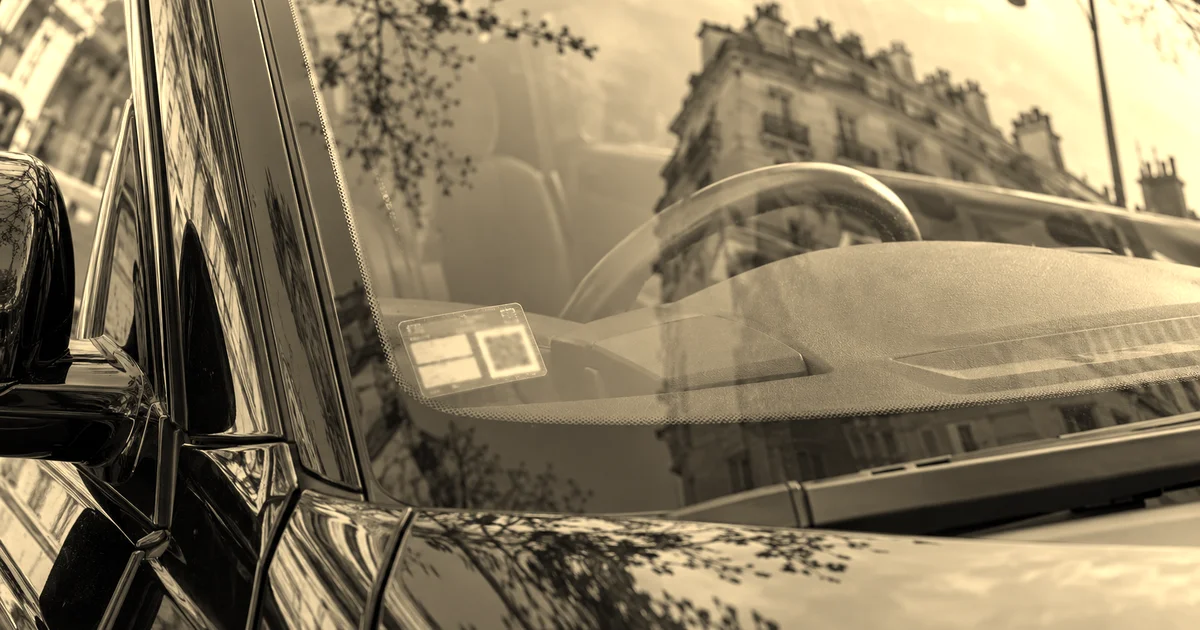 Angle inférieur gauche du pare-brise d'une berline noire portant la vignette de voiture de transport avec chauffeur, traitement sépia presse B2B