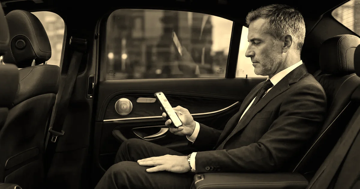 Business passenger checking his phone in the rear seat of an executive sedan, sepia B2B press treatment
