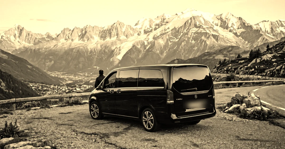 Mercedes Classe V sur une route alpine face au massif du Mont-Blanc au couchant, village de vallée en contrebas, traitement sépia presse B2B